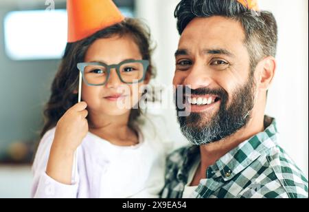 Père, fille et portrait avec chapeaux d'anniversaire pour la célébration avec des lunettes, heureux et accessoires pour la décoration à la maison. Famille, enfant et papa à la fête Banque D'Images