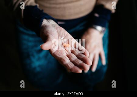Gros plan de la main de la femme âgée montrant quelques pilules, soulignant l'importance des médicaments dans sa routine quotidienne. Banque D'Images
