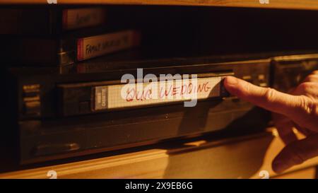 Gros plan d'une personne insérant une cassette VHS dans un lecteur avec des images nostalgiques de mariage de la caméra vidéo à domicile. Technologie rétro des années 90. Ancien magnétoscope avec faible profondeur de champ et Bokeh. Banque D'Images