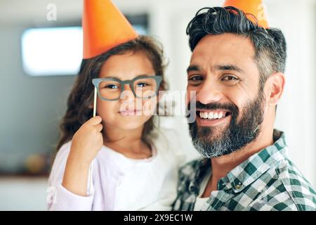 Père, enfant et portrait avec chapeaux d'anniversaire pour la célébration avec des lunettes, heureux et accessoires pour la décoration à la maison. Famille, fille et papa à la fête Banque D'Images