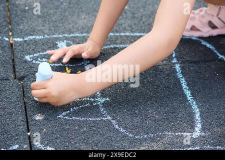 Fille méconnaissable dessinant sur le sol avec des craies colorées. Banque D'Images