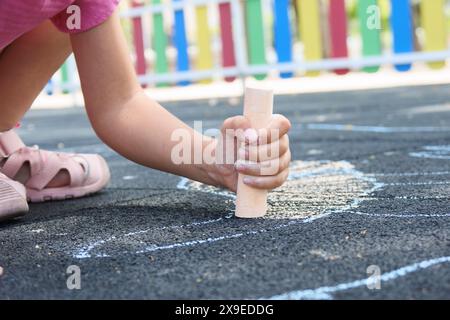 Fille méconnaissable dessinant sur le sol avec des craies colorées. Banque D'Images