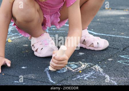 Fille méconnaissable dessinant sur le sol avec des craies colorées. Banque D'Images