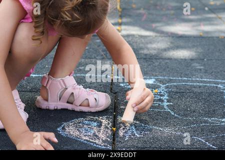 Fille méconnaissable dessinant sur le sol avec des craies colorées. Banque D'Images