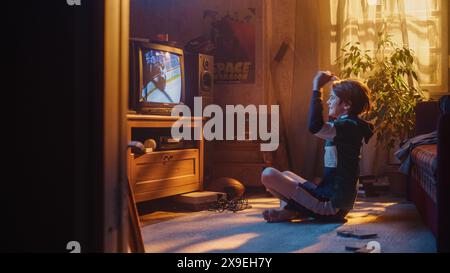 Concept d'enfance rétro nostalgique. Jeune garçon regarde le match de hockey à la télévision dans sa chambre avec l'intérieur daté. Soutenir son équipe préférée et s'exciter lorsque les joueurs marquent un but. Banque D'Images