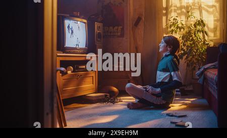 Concept d'enfance rétro nostalgique. Jeune garçon regarde le match de hockey à la télévision dans sa chambre avec l'intérieur daté. Soutenir son équipe préférée et être excité quand les joueurs professionnels marquent un but. Banque D'Images