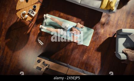 Vue de dessus Sport : Guy attrayant faisant du yoga s'étirant sur un tapis d'exéricise à la maison. Musclé et beau homme athlétique fait un entraînement de fitness dans son élégant appartement. Vue descendante de Cozy Living Room. Banque D'Images