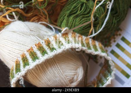 Photographie rapprochée du projet de tricot Fair Isle sur les aiguilles en cours avec des boules de fil d'alpaga fines blanches, jaunes et vertes Banque D'Images