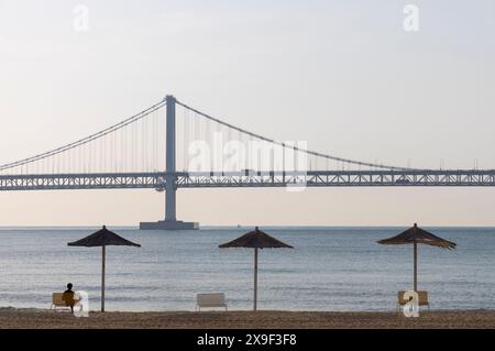 Homme assis sur la plage de Gwangalli avec le pont de Gwangan en arrière-plan, Busan, Corée du Sud Banque D'Images