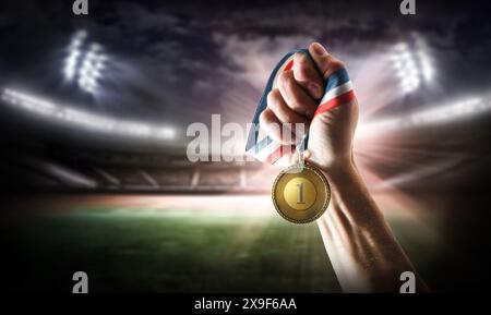 Main montrant la médaille d'or avec le numéro gravé 1 et stade d'athlétisme derrière la nuit Banque D'Images