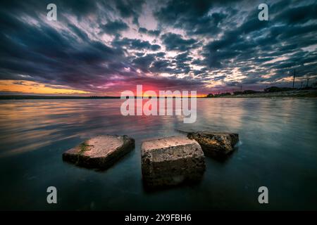 Trois pierres submergées dans le golfe de Curonien sous un ciel sombre de coucher de soleil, Lituanie Banque D'Images