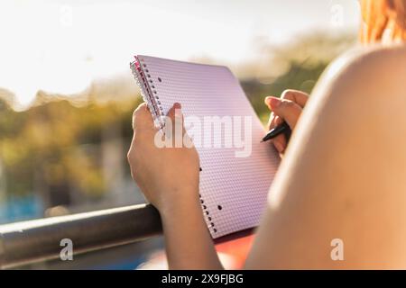 Femme écrivant dans un cahier lors d'une session d'étude en plein air au coucher du soleil - concentration et concentration, mode de vie sain, journée lumineuse et ensoleillée, active et d. Banque D'Images