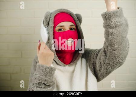 Femme en Balaclava rose dansant contre un mur de briques blanches Banque D'Images