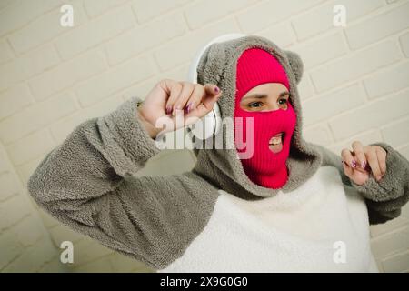 Femme en Balaclava rose dansant contre un mur de briques blanches Banque D'Images