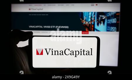 Personne tenant le téléphone portable avec le logo de la société vietnamienne de gestion d'investissement VinaCapital en face de la page Web de l'entreprise. Concentrez-vous sur l'affichage du téléphone. Banque D'Images