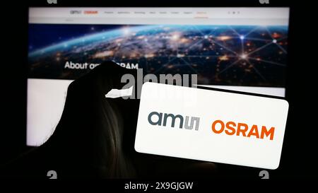 Personne tenant le téléphone portable avec le logo de la société autrichienne d'électronique AMS OSRAM AG en face de la page Web de l'entreprise. Concentrez-vous sur l'affichage du téléphone. Banque D'Images