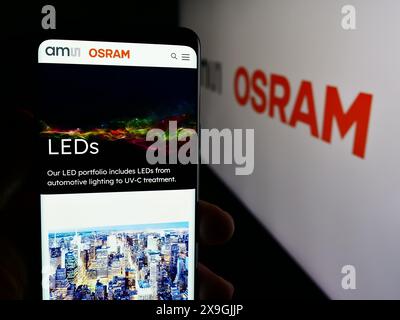 Personne tenant le téléphone portable avec la page Web de la société autrichienne d'électronique AMS OSRAM AG devant le logo de l'entreprise. Concentrez-vous sur le centre de l'écran du téléphone. Banque D'Images