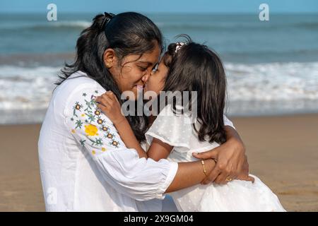 Un moment chaleureux capturé sur la côte ensoleillée : une fille embrasse affectueusement sa mère sur fond de vagues qui s'écrasent. Banque D'Images