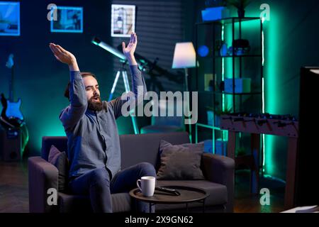 Jolly Man applaudissant des mains après que son équipe favorite a gagné tout en regardant un événement sportif en direct diffusé à la télévision. Heureux supporter applaudissant son propre club, profitant de la victoire de la compétition de football Banque D'Images