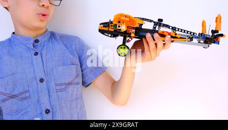 enfant, garçon de 10 ans joue avec un avion orange de lego parts, constructeur dans les mains des enfants gros plan, jouet éducatif, développement de concept Banque D'Images