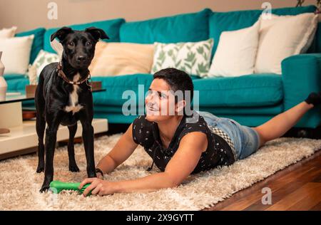 femme joyeuse aux cheveux courts partage un moment joyeux avec son chien bien-aimé, s'engageant dans une interaction ludique sur le sol confortable de leur confortable liv Banque D'Images