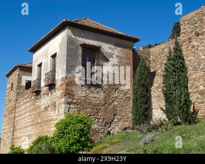 Une vieille maison à l'intérieur d'une forteresse avec des murs de pierre et des cyprès sous un ciel bleu clair, la ville de Malaga sur la mer Méditerranée avec l'historique Banque D'Images