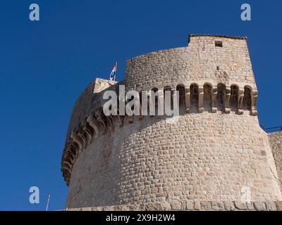 Forteresse en pierre massive avec drapeau sur un ciel bleu, la vieille ville de Dubrovnik avec des maisons historiques, des églises, des toits rouges et des murs de forteresse Banque D'Images