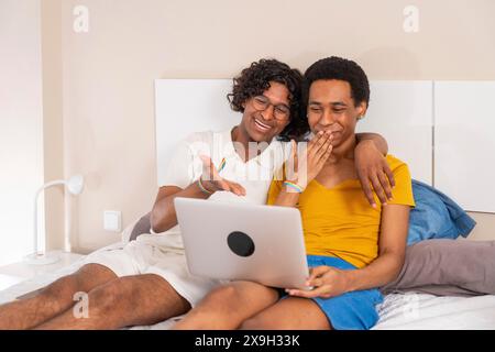 Jeune couple gay masculin latin s'amusant en utilisant un ordinateur portable dans le lit Banque D'Images