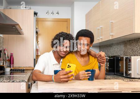 Couple adulte latin gay partageant un téléphone mobile tout en buvant un café du matin à la maison Banque D'Images