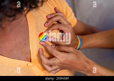 Gros plan d'un homme gay qui épingle un badge LGBT sur son couple assis sur le canapé Banque D'Images