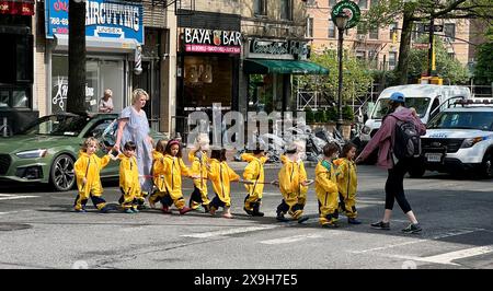 Les enfants de l'école maternelle dans des sauteurs étanches jaune vif un jour de printemps traversent la rue pour se rendre à Prospect Park dans le quartier Windsor Terrace de Brooklyn, New York. Banque D'Images