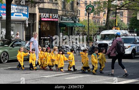 Les enfants de l'école maternelle dans des sauteurs étanches jaune vif un jour de printemps traversent la rue pour se rendre à Prospect Park dans le quartier Windsor Terrace de Brooklyn, New York. Banque D'Images