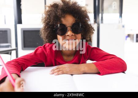 À l'école, jeune étudiant biracial portant des lunettes de soleil assis à un bureau dans la salle de classe Banque D'Images