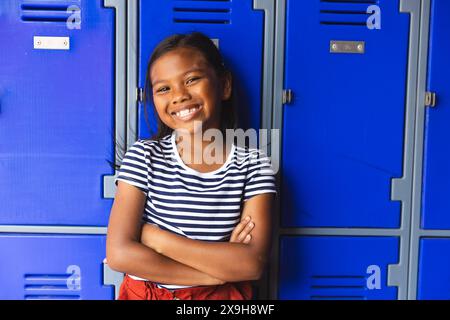 À l'école, une jeune étudiante biraciale est debout dehors, les bras croisés, souriante Banque D'Images