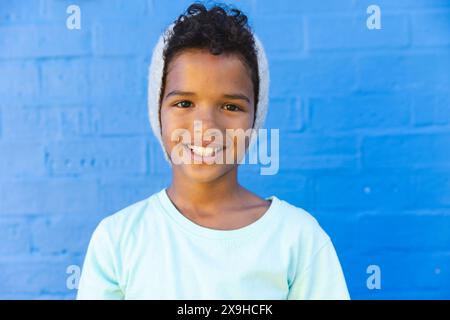 Garçon biracial sourit brillamment contre un mur bleu Banque D'Images