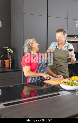 Diverses amies seniors cuisinant, riant ensemble à la maison Banque D'Images