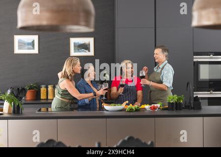 Diverses amies seniors tenant des verres à vin, riant à la maison Banque D'Images