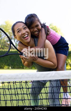 En plein air, mère biraciale et fille souriante avec des raquettes de tennis sur le court Banque D'Images