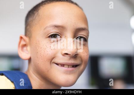 Garçon biracial avec des taches de rousseur sourit chaleureusement dans une salle de classe d'école, ses yeux bruns brillants Banque D'Images