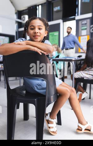 Fille biraciale dans une salle de classe s'assoit tranquillement sur une chaise, regardant la caméra Banque D'Images