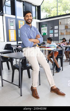 Professeur masculin asiatique en chemise bleue et pantalon bronzé souriant, debout en classe Banque D'Images