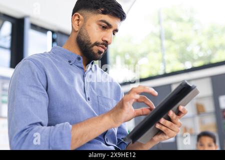 À l'école, enseignant asiatique utilisant une tablette en classe, un étudiant biracial masculin regardant Banque D'Images