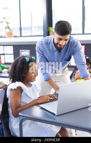 Un jeune professeur asiatique aide une fille biraciale avec son travail informatique Banque D'Images