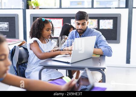 Un jeune professeur asiatique aide une fille biraciale avec son ordinateur portable Banque D'Images