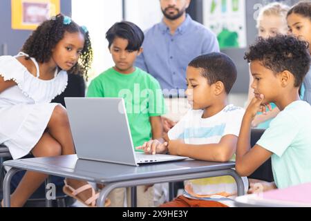 À l'école, dans la salle de classe, un groupe diversifié de jeunes étudiants se concentrant sur un ordinateur portable Banque D'Images