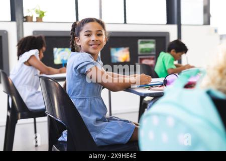 À l'école, une jeune fille biraciale aux cheveux bruns bouclés est assise, souriant à la caméra Banque D'Images