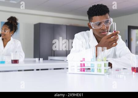 Adolescent biracial garçon et fille mener une expérience dans un laboratoire de lycée. Vêtus de blouses de laboratoire, ils se concentrent intensément sur leur tâche scientifique à portée de main. Banque D'Images