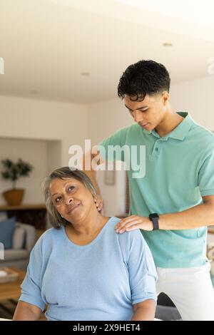 À la maison, jeune physiothérapeute masculin biracial traitant la patiente senior. Espace lumineux avec sièges confortables et lumière naturelle remplissant la salle, cre Banque D'Images