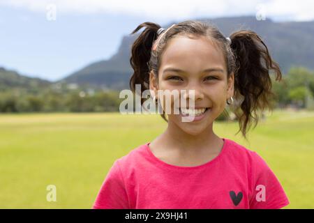 Fille biraciale avec un sourire lumineux, portant une chemise rose avec un design de coeur, avec un espace de copie Banque D'Images