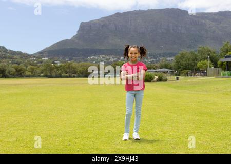 Fille biraciale se tient en toute confiance dans un parc avec des montagnes en arrière-plan, avec un espace de copie Banque D'Images